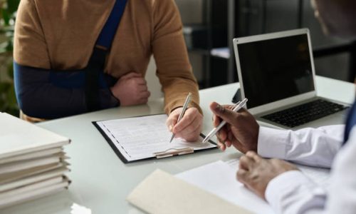 Close up of man filling in medical insurance form, injured hand in sling in background, copy space